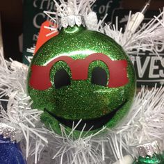 a green ornament with a red mask on it's face and white tinsel