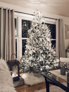 a living room with a christmas tree in the center and windows behind it, all lit up