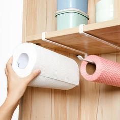 a person holding a roll of toilet paper in front of a wooden shelf with two cups on it