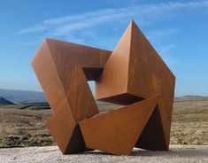 a large metal sculpture sitting on top of a dirt field next to a dry grass field