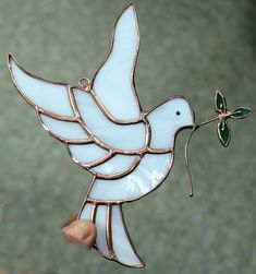 a hand holding a stained glass bird ornament with a small green leaf on it