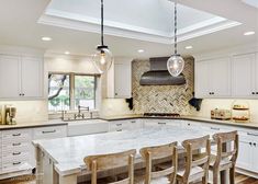 a large kitchen with white cabinets and marble counter tops, along with wooden dining chairs