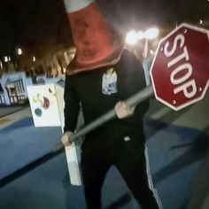 a man holding a stop sign on the side of the road at night with one hand in his pocket