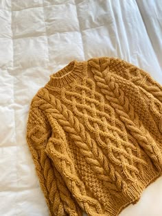 a brown knitted hat laying on top of a white bed sheet covered in blankets