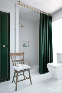 a white toilet sitting next to a green curtain in a bathroom on top of a wooden chair