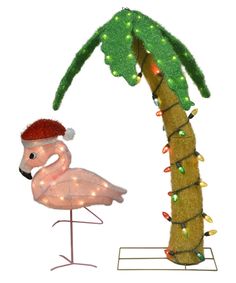 a pink flamingo standing next to a palm tree with christmas lights on it's branches