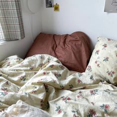 an unmade bed in a small room with white walls and floral bedspread