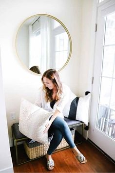 a woman sitting on a bench in front of a mirror holding a pillow and looking at it