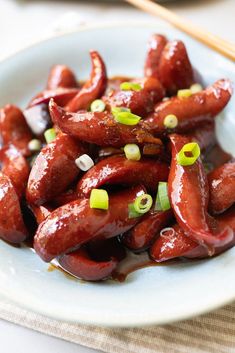 a white plate topped with hot dogs covered in ketchup and green onions next to chopsticks