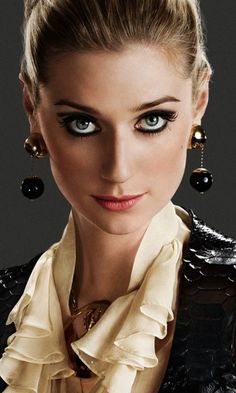 a woman with blue eyes wearing black and gold jewelry