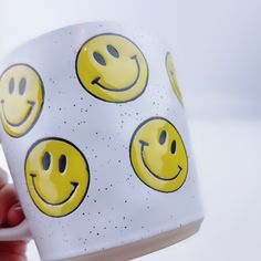 a hand holding a coffee mug with smiley faces on it