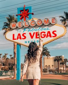 a woman standing in front of the welcome to fabulous las vegas sign with her arms up