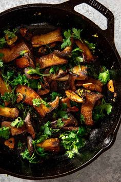 a skillet filled with cooked mushrooms and parsley on top of a gray table