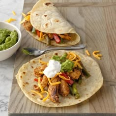 two tacos with chicken, peppers and guacamole on a cutting board