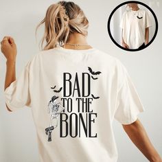 Saddle up for a spooky season with our trendy western Halloween "Bad to the Bone' t-shirt. This comfort colors graphic tee features a cute halloween bat on the front and a cool cowboy skeleton leaning against the words printed on the back. Embrace your inner cowgirl and add a little western flair to your Halloween wardrobe. Whether you're heading to a fall festival or a Halloween hoedown, this shirt is perfect for you and all your ghoul friends! Comfort Colors garment-dyed t-shirt is made of 100% with ring-spun cotton. The soft-washed, garment-dyed fabric brings extra coziness to your wardrobe while the relaxed fit makes it an excellent daily choice. The double-needle stitching throughout the tee makes it highly durable while the lack of side-seams helps the shirt retain its tubular shape. Halloween Hoedown, Cowboy Skeleton, Skeleton Cowboy, Gifts For Halloween, Western Halloween, Cowboy Shirt, Cowgirl Shirts, To The Bone, Bad To The Bone