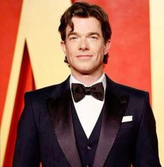 a man in a tuxedo and bow tie at an oscars event with his hands in his pockets