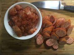 a wooden cutting board topped with a bowl of meat and sliced carrots next to a knife