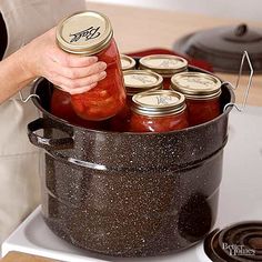 a person holding a jar full of pickles on top of a stove with the lid open