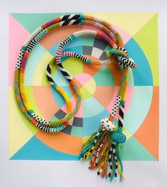 a multicolored necklace with tassels is displayed on a brightly colored background