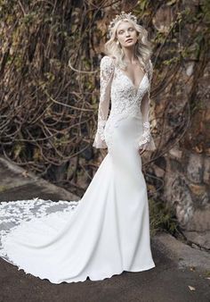 a woman in a white wedding dress standing next to a stone wall with ivy growing on it