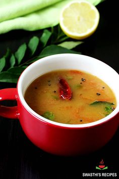 a red bowl filled with soup on top of a wooden table next to a slice of lemon