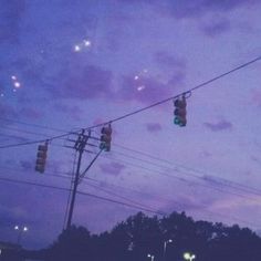 two traffic lights hanging from wires in the sky at night with clouds and trees behind them