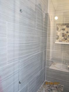 a bathroom with gray tile and stone flooring on the shower wall, along with a white toilet