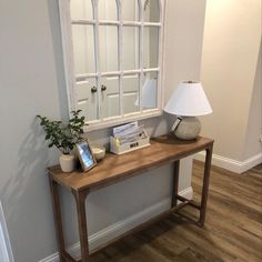 a wooden table with a lamp on top of it next to a mirror and window