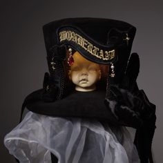 A hat with a strange doll's head placed in the middle. It features a tall crown and is decorated with lace embroidery and ribbons. Let yourself be invited to a mysterious and dark world. 
 
 

 

 
 
 
 Size 
 
 Height: 14cm 
 Diameter: 17cm (*Size not including brim) 
 Diameter: 24cm (*Size including brim) 
 
 
 Material 
 
 Polyester 
 velvet Whimsical High Crown Hat For Themed Events, Whimsical Costume Hat With Tall Crown For Costume Party, Whimsical Costume Hat With Tall Crown For Parties, Whimsical Tall Crown Costume Hat For Costume Party, High Crown Hats For Halloween Themed Events, Halloween High Crown Hat For Themed Events, Victorian High Crown Costume Hat, Victorian Curved Brim Costume Hat, Carnival Costume Top Hat With High Crown