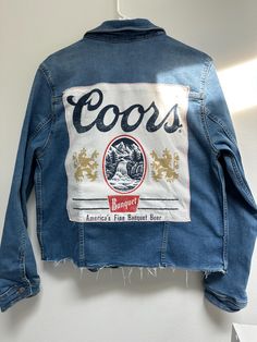 Show off some Beer Love in this one-of-a-kind frayed bottom jean jacket! Perfect for concerts or anything where you want to be UNIQUE! Women's Large stretch jean jacket with cream Coors tee sewn on back. 3 gold glitter stars on front for some bling! Size: Women's L Chest: 20.5" armpit to armpit Arm Length: 24.5" shoulder to hem Back Length: 23.5" top of collar to hem Color: medium wash  All clothing is pre-washed & comes from a smoke-free home. Wash gentle cycle, cold water, inside out to protect stars  Tumble dry low Don't iron over graphic tee Please check measurements, sizing differs between brands. Keep in mind items are perfectly imperfect and made with love!! *I do not own the rights or designs to the shirts- these are repurposed shirts* Grunge Cotton Outerwear With Frayed Hem, Cotton Denim Jacket With Frayed Hem For Streetwear, Grunge Cotton Outerwear With Patches, Cotton Grunge Outerwear With Patches, Concert Jacket, Unique Jeans, Gold Glitter Stars, Distressed Jean Jacket, Upcycle Jeans