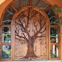 an open wooden door with a tree painted on the front and side glass panels above it