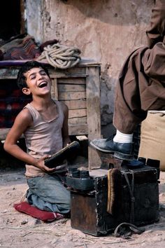 a young boy laughing while sitting on the ground with his feet up in front of him