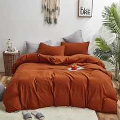 a bed with an orange comforter in a bedroom next to a potted plant