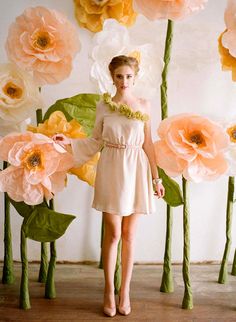 a woman standing in front of giant paper flowers with leaves and petals around her body