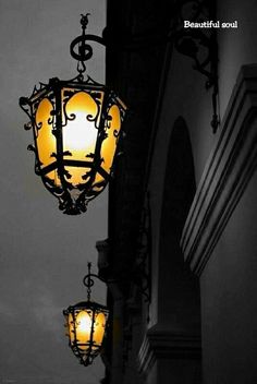 an old fashioned street light hanging from the side of a building in black and white