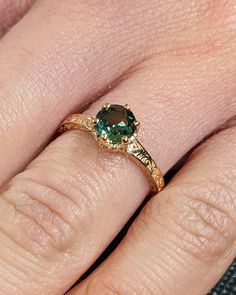 a woman's hand with a green ring on top of her finger and an emerald stone in the middle