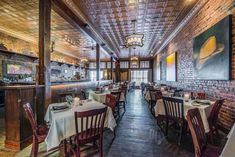 an empty restaurant with wooden tables and white tablecloths on the tables, along with brick walls