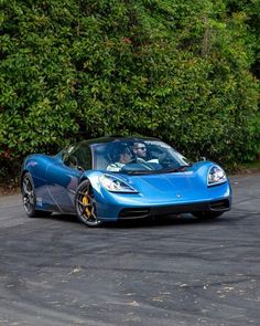 a blue sports car driving down a road next to green bushes and trees in the background