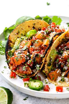 two tacos on a plate with limes and cilantro