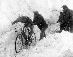 two men on bicycles in the snow with another man standing next to them looking at something