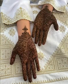 two hands with henna designs on them sitting on a tablecloth covered in gold and white cloths