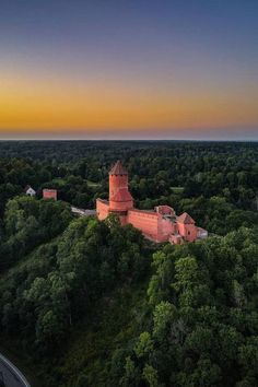 an aerial view of a castle in the middle of trees at sunset, with a road running through it