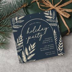 a holiday party card with gold foil on it next to a present box and evergreen branches