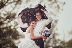 a bride and groom are holding an umbrella in the rain as they pose for a photo