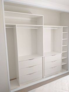 an empty white closet with shelves and drawers on the wall next to a bed in a room