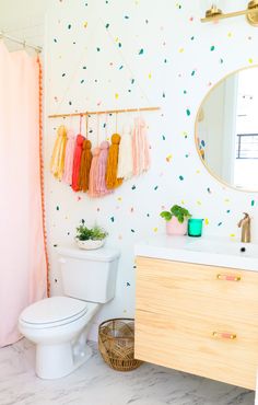 a white toilet sitting next to a bathroom sink under a mirror and a wooden cabinet