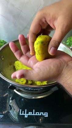 a person holding something in their hand over a metal bowl with yellow substance on it