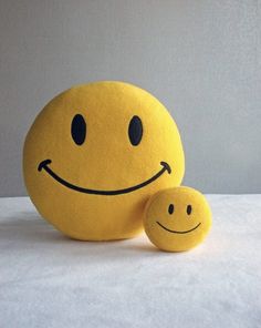 a yellow smiley face pillow sitting on top of a white table next to a smiling face