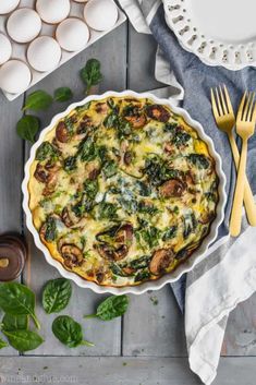 an egg dish with spinach, mushrooms and cheese in a pie pan next to eggs