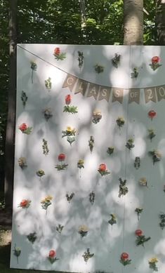 a sign with flowers on it in the woods next to a tree and two people's faces